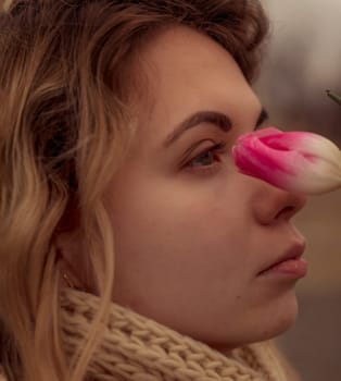close-up of a blonde with a flower near her face. portrait of a girl, near her face she holds one pink tulip. she stands in profile