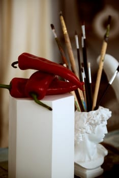 three large red peppers and a glass for brushes in the form of an antique head. hot red pepper and classic