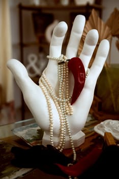 plaster hand holding pearl necklace and red hot pepper. close-up hand made of white plaster, paint brushes nearby. concept hot classic, white and red