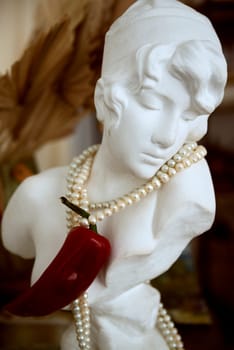 bust of a plaster girl with pearls and red hot peppers on her neck. red on white