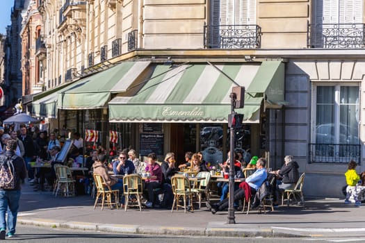 Many people are sitting at tables in a cafe. Street with terrace cafe. Paris, France - October 20, 2024