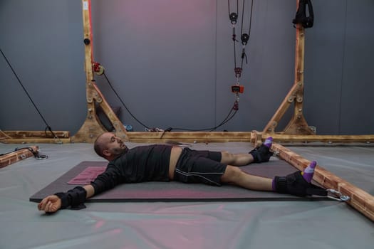 Caucasian man lying on a mat, undergoing spinal decompression therapy with weights and pulleys attached to his ankles and wrists