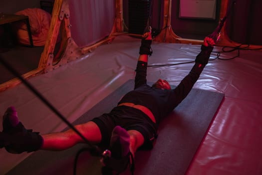 Sportsman exercising with suspension straps, enhancing strength and flexibility in a unique pink lit fitness environment