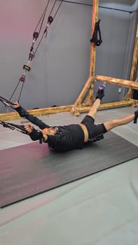 Sportsman exercising with suspension training equipment, performing a fly exercise on a mat