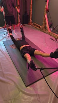 Male athlete exercising with suspension straps guided by personal trainer in modern neon lit gym