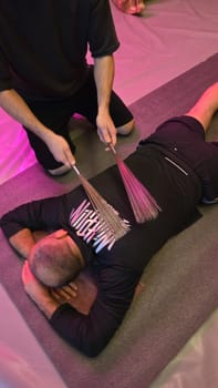 The therapist gives a back massage with metal rods to a patient lying on a mat
