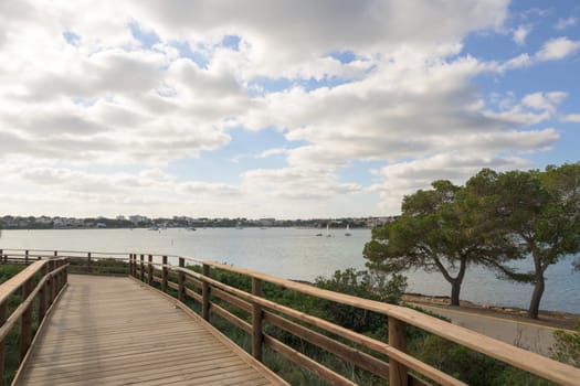 wooden boardwalk in a coastal bay with the fishing village in the background on a cloudy day Mallorca ,Balearic Islands, Spain