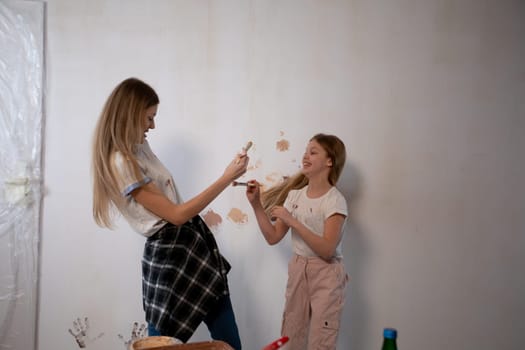 Two lively and playful girls joyfully engage in painting a wall together, as they bond and create lasting memories