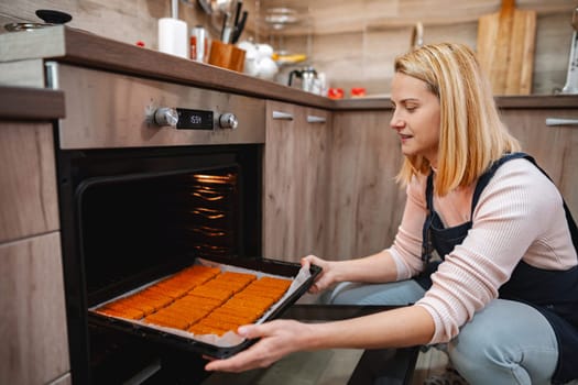 A young woman carefully removes a tray of freshly baked goods from the oven.