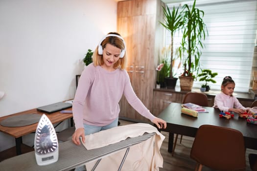 Woman listens to music while ironing clothes in a bright living space.
