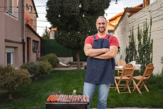 Grill master stands proudly in a lush backyard while cooking delicious sausages.