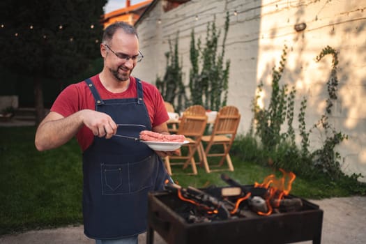 A joyful cook prepares sausages on the grill, surrounded by friends and nature.