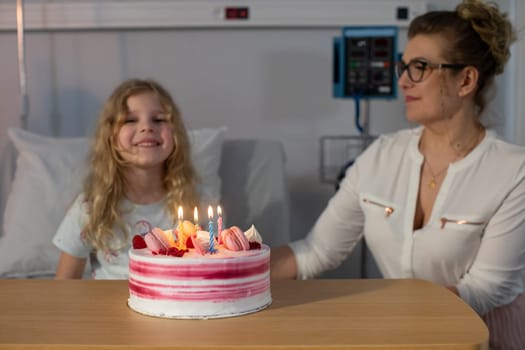 A cheerful girl celebrates her birthday with a cake and colorful candles in a warm, caring hospital