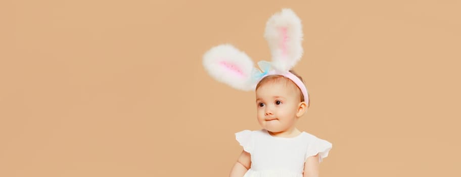 Portrait of cute baby with easter rabbit ears sitting on brown studio background