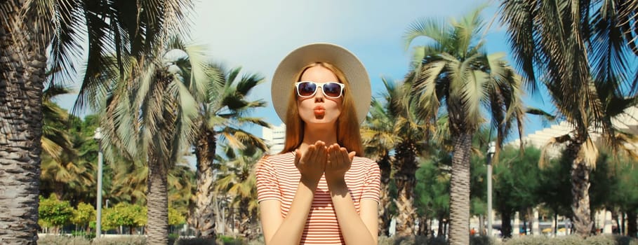 Portrait of beautiful young woman in summer park wearing straw tourist hat, sunglasses against a palm trees background