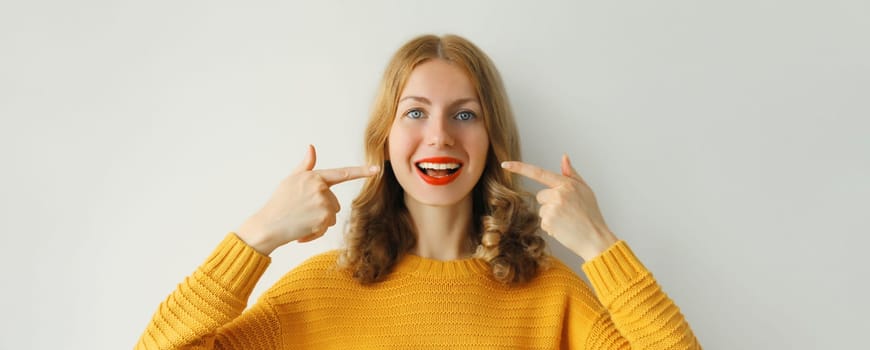 Portrait of happy smiling young woman points with fingers to her white clean teeth showing smile on white background