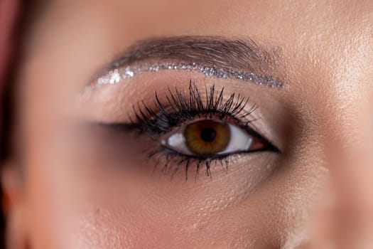 A striking closeup of an eye highlights elegant makeup with glitter and intricate eyeliner artistry