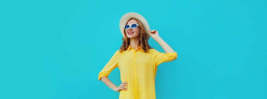 Beautiful young woman posing wearing summer straw hat, yellow shirt looking away on blue studio background