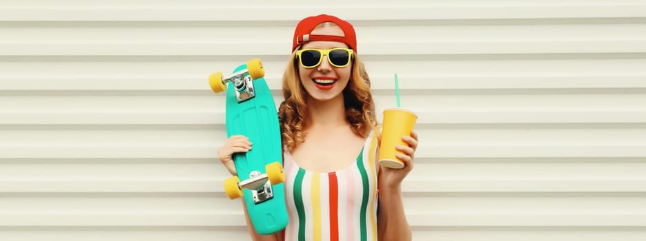 Summer portrait of happy cheerful stylish young woman with skateboard and cup of fresh juice in colorful clothes standing on white background