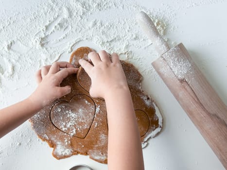 Child shaping heart cookies on floured surface with rolling pin.