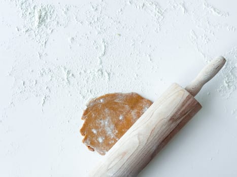 Rustic wooden rolling pin on floured surface with cookie dough.