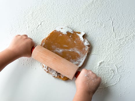 Child rolling dough on floured surface with rolling pin.