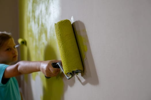A child happily paints a wall with a bright green roller, displaying creativity and enhancing the home