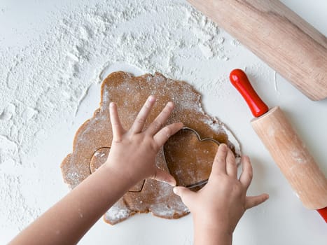 Child cutting heart shaped cookie dough with wooden rolling pins.