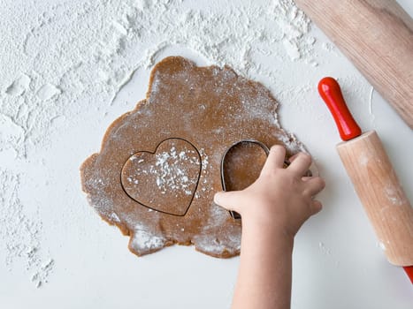 Child making heart shaped cookies with dough and rolling pin.