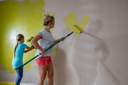 Two women enthusiastically painting a wall with bright yellow color, showcasing teamwork and creativity.