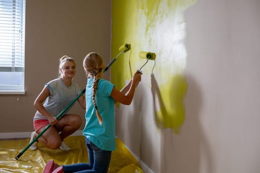 Two kids are joyfully and creatively painting a wall a bright yellow color, showcasing their teamwork and imagination