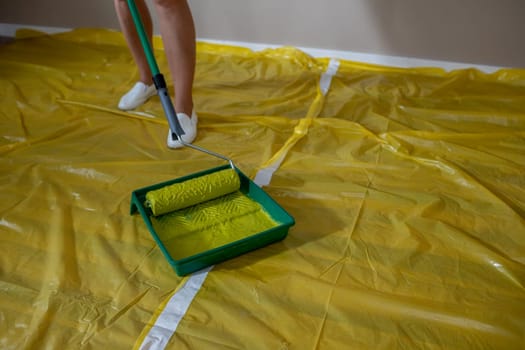 A detailed closeup image of a vibrant painting in progress, showcasing a paint roller on a yellow tarp surface