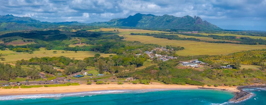 Aerial view of Kauai Island, Hawaii, showing a golden sandy beach, turquoise waters, a coastal community, lush greenery, and the Napali cliffs.