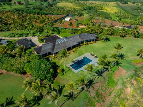 Aerial image of a modern house on Kauai Island, Hawaii, featuring a dark roof, skylights, a rectangular pool, manicured lawn, and lush greenery.
