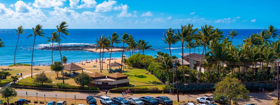 Golden sand beach on Kauai island, Hawaii, featuring clear waters, a lagoon, swaying palms, picnic areas, a parking lot, and lush tropical greenery.
