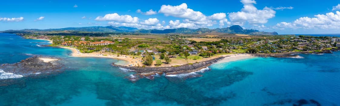 Aerial view of Kauai island's Hawaii coastline with sandy beaches, turquoise waters, rocky outcrops, residential areas, lush greenery, and mountain ranges.