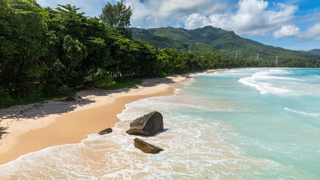 Waves gently wash onto a secluded sandy beach bordered by dense green forest. Grand Anse. Seychelles, Mahe.