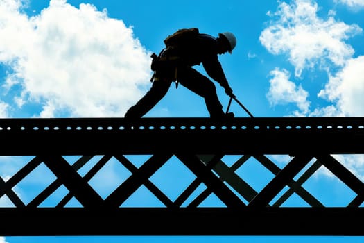 A man is working on a bridge, and the sky is blue. The man is wearing a hard hat and a harness