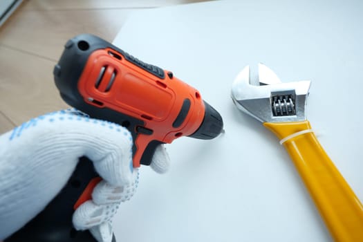 A person operates a power drill while an adjustable wrench is nearby.