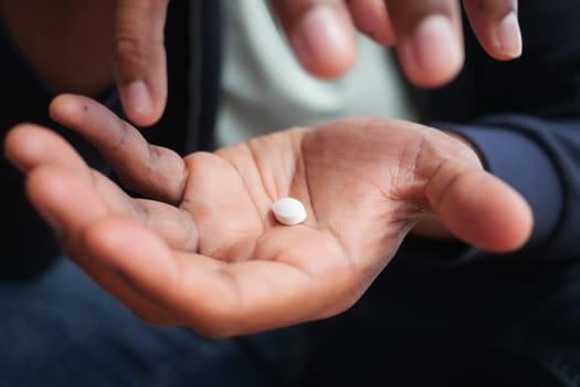 A person examines a white pill in their palm, deep in thought.