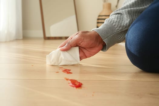 A person uses a paper towel to clean sauce from the floor.