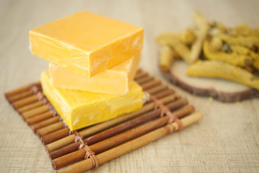 Yellow soap bars are neatly stacked on a bamboo mat beside dried herbs.