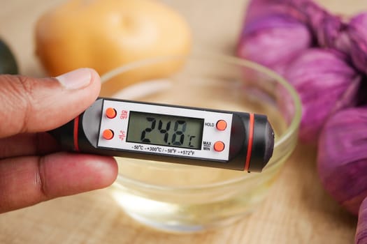 Hand Holding Digital Thermometer Measuring Temperature of oil in Glass Bowl.