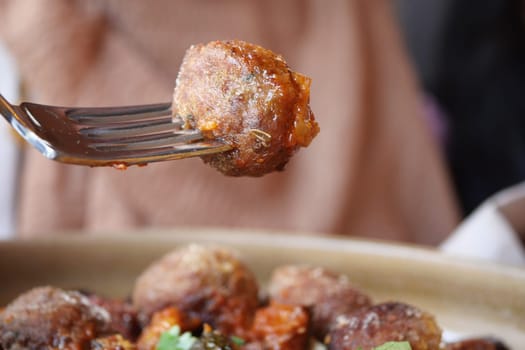 A juicy meatball is held up by a fork, showcasing its texture and sauce.