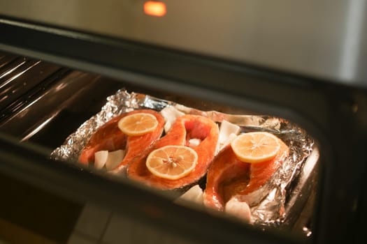 Fresh salmon fillets are baking in the oven with lemon slices on top.