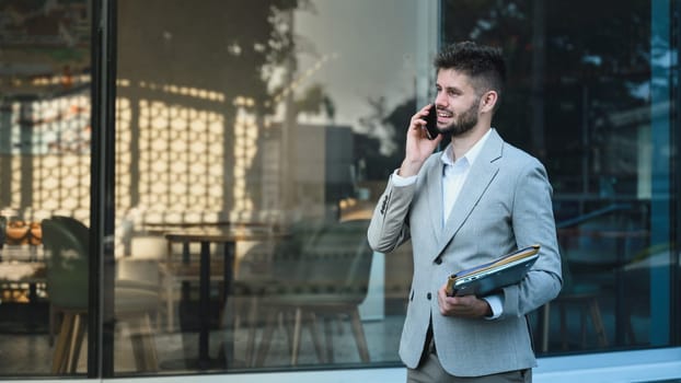 Caucasian businessman having phone conversation standing outside contemporary glass building.