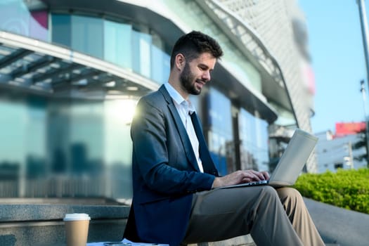 Smiling caucasian businessman working on his laptop in a contemporary cityscape.