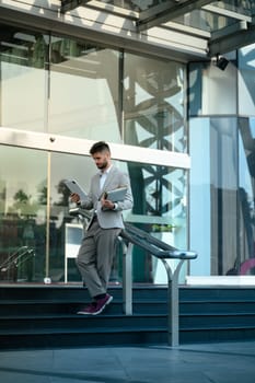 Professional businessman standing outside a contemporary glass building and using digital tablet.