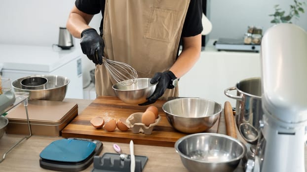 Man in black gloves whisking ingredients in stainless steel bowl for cookie dough.