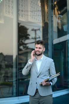 Caucasian businessman having phone conversation standing outside contemporary glass building.